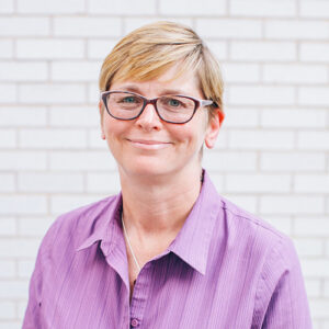 Headshot of Tari Hanneman wearing a purple shirt and glasses. She talks about the Healthcare Equality Index in the article.