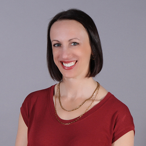 Woman in a red short sleeve shirt smiling against a solid grey background.